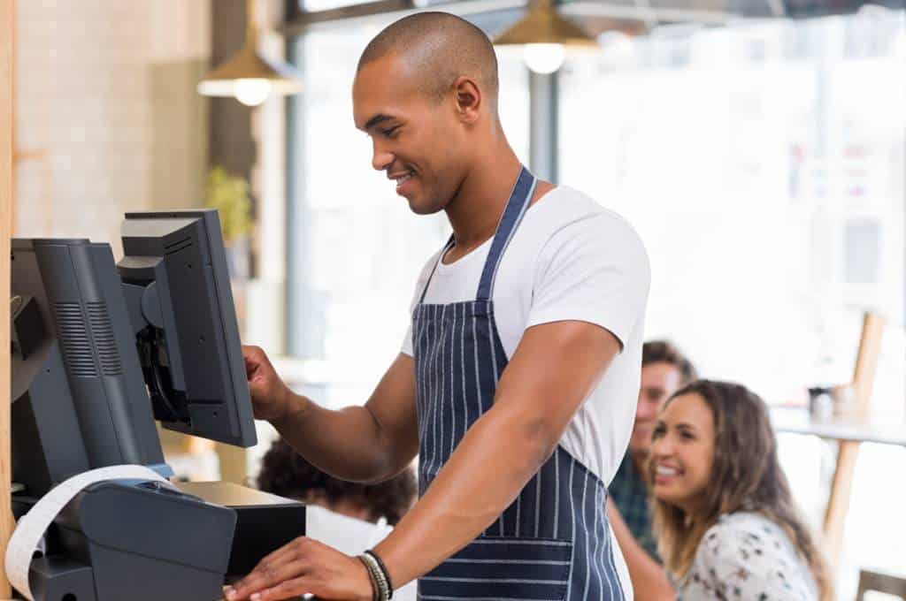 Un commerçant portant un tablier travaillant à une caisse enregistreuse tactile dans un restaurant.