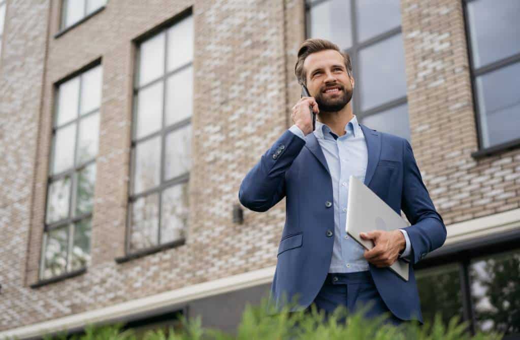 Un homme d'affaires en costume passe un appel téléphonique d'investissement immobilier bien informé alors qu'il se tient devant un immeuble.